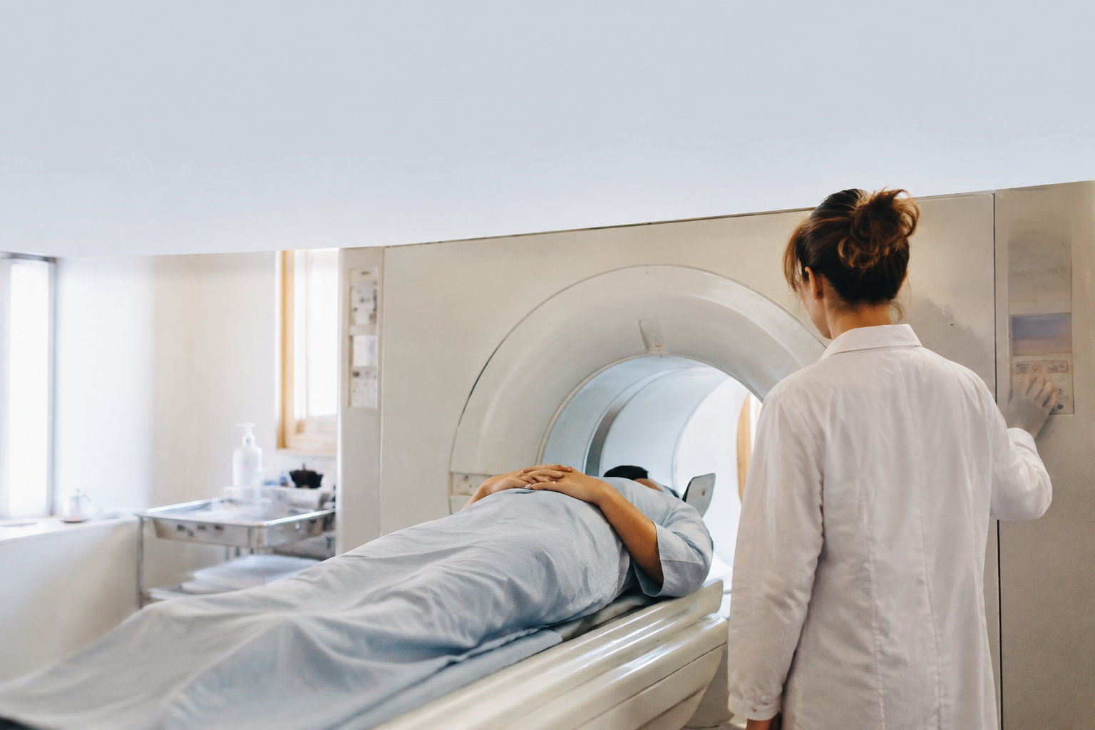 Une technicienne en blouse blanche utilise une machine de scanner avec un patient allongé.