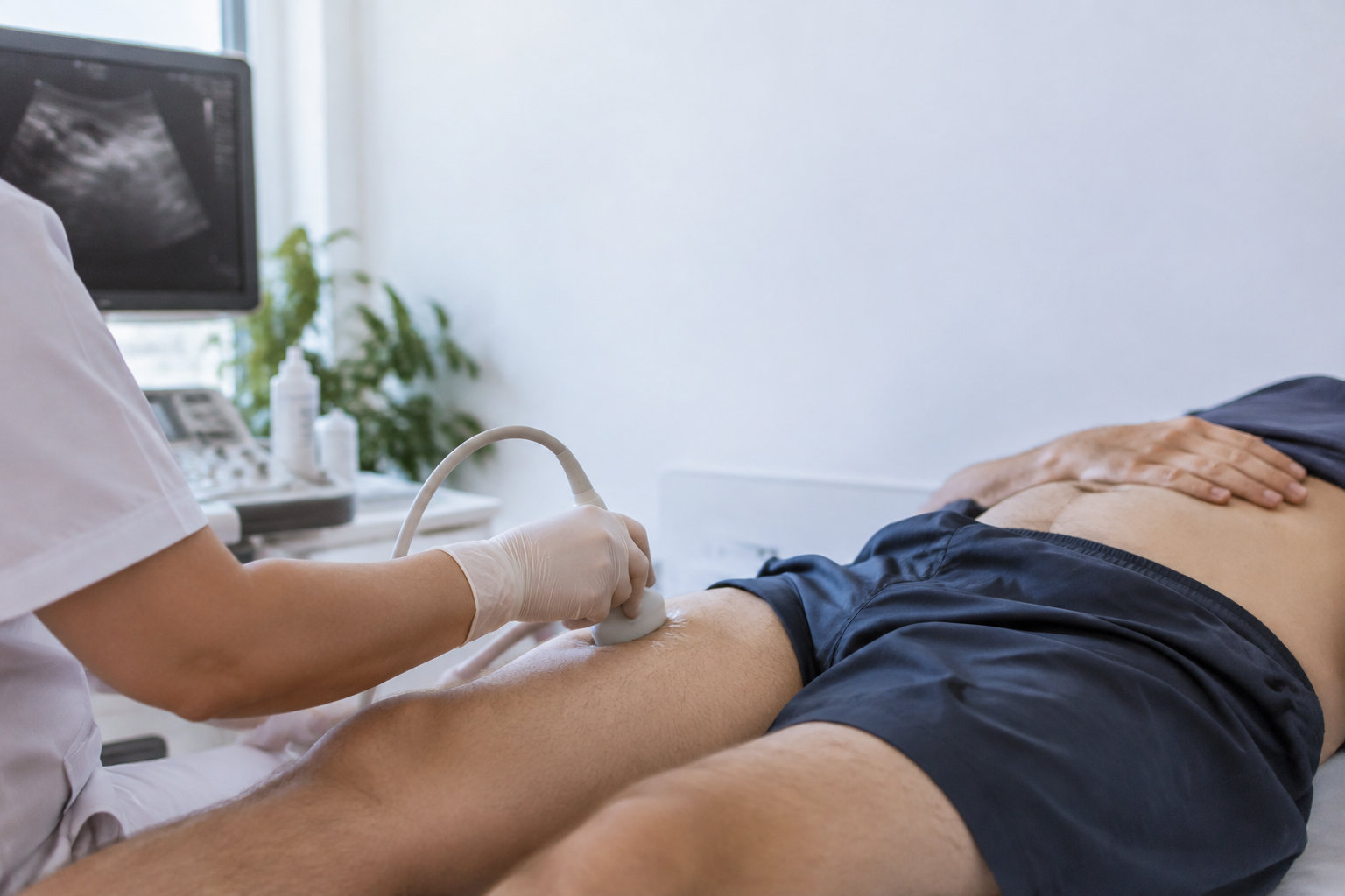 Un médecin effectue une échographie de la région inguinale sur un patient allongé sur une table d'examen.